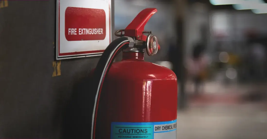 A bright red fire extinguisher mounted on a wall next to a white sign with red lettering
