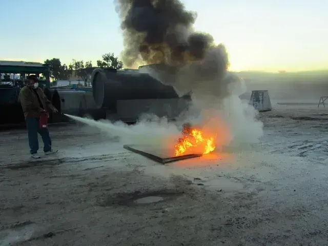A person using a fire extinguisher to put out a small fire on the ground outdoors