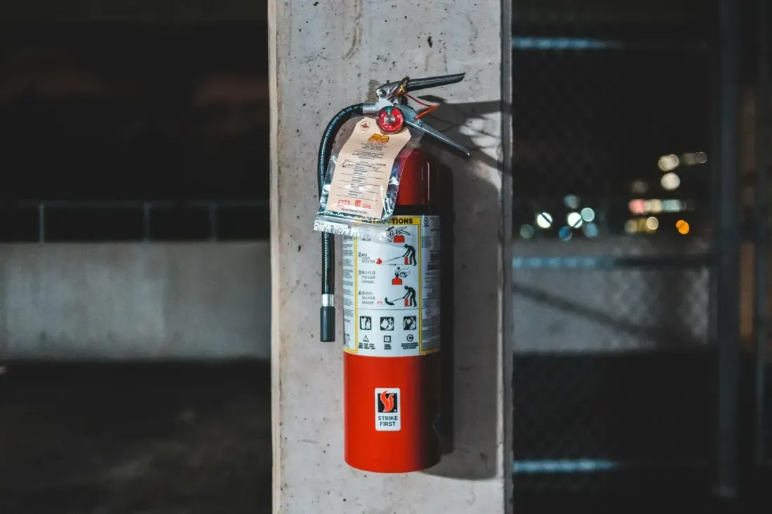 A red fire extinguisher with a maintenance tag mounted on a concrete pillar in an industrial setting